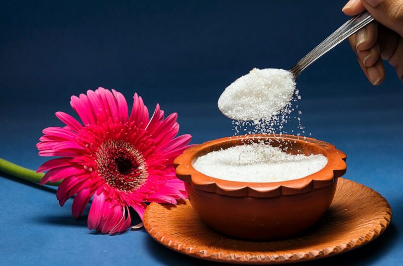 Spoon pouring sugar into a bowl with flower.