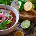 a bowl of chili soup with limes and cilantro